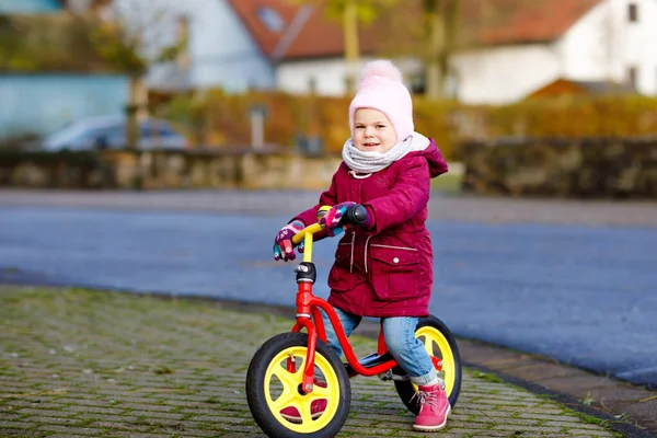 Linda niña pequeña montando en bicicleta de equilibrio de carrera a la guardería, escuela de juegos o jardín de infantes. Feliz niño bebé encantador sano que se divierte con el aprendizaje en bicicleta más magra. Niño activo en el día frío al aire libre . —  Fotos de Stock