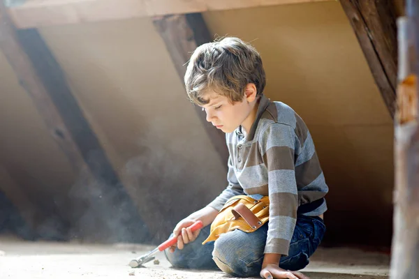 Menino adorável ajudando com ferramentas de brinquedo no local de construção. Criança engraçada de 6 anos se divertindo na construção de uma nova casa de família. Criança com unhas e martelo ajudando o pai a renovar a casa velha . — Fotografia de Stock