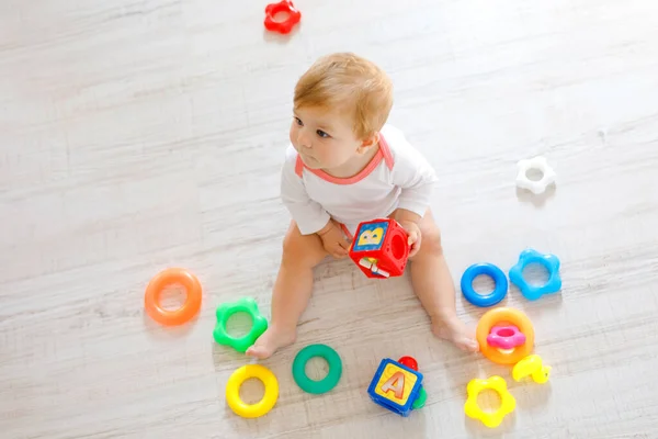 Чарівна дівчинка грає з освітніми іграшками в дитячій кімнаті. Щаслива здорова дитина розважається з різними барвистими іграшками вдома. Малюк намагається побудувати пластикову піраміду і використовує блоки з літерами — стокове фото