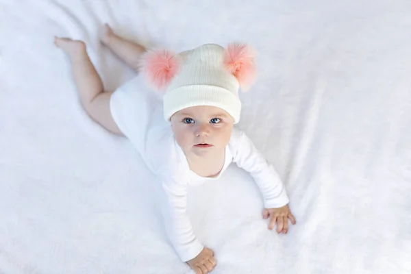 Niedliche entzückende Baby-Kind mit warmen weißen und rosa Hut mit niedlichen Noppen. Glückliches kleines Mädchen, das Krabbeln lernt und in die Kamera schaut. Nahaufnahme für Weihnachtsurlaub und Familienkonzept.. — Stockfoto