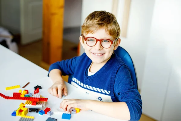 Niño rubio con anteojos jugando con muchos bloques de plástico de colores. Adorable niño de la escuela que se divierte con la construcción y la creación de robot. Ocio creativo moderna técnica y robótica. — Foto de Stock