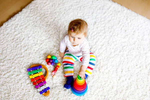 Чарівна мила красива маленька дівчинка, яка грає з освітніми іграшками вдома або в дитячій кімнаті. Щаслива здорова дитина розважається з барвистою дерев'яною іграшковою пірамідою дощовика. Малюк вивчає різні навички — стокове фото