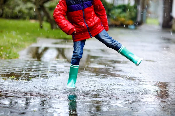 小孩穿着黄色雨靴的特写，在雨夹雪中散步，在寒冷的日子里。穿着五颜六色休闲装的孩子跳进水坑里.在户外玩的开心 — 图库照片