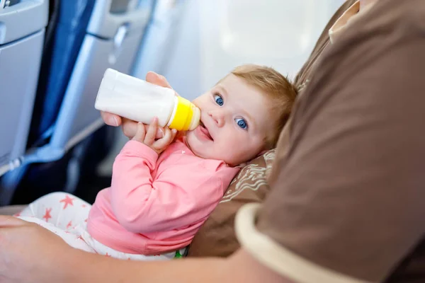 Padre che tiene in braccio la figlioletta durante il volo in aereo in vacanza. Bambina che beve latte artificiale dalla bottiglia. Viaggio aereo con bambino, bambino e concetto di famiglia. Uomo stanco in viaggio con i bambini . — Foto Stock