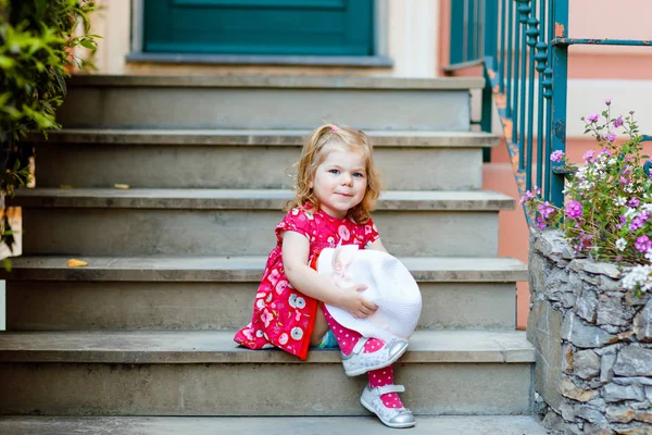 Porträtt av vacker liten gorgeus härlig småbarn flicka i rosa sommar titta kläder, mode klänning, knästrumpor och hatt. Glad frisk baby barn poserar framför färgglada hus. — Stockfoto