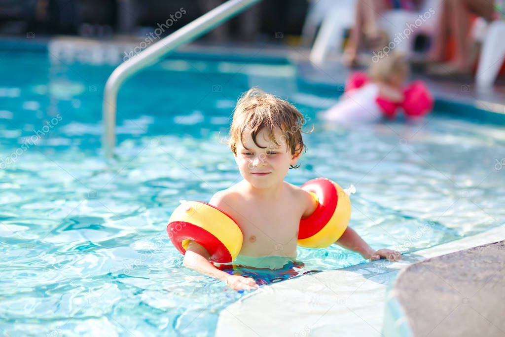 Happy little kid boy having fun in an swimming pool. Active happy healthy preschool child learning to swim. with safe floaties or swimmies. Family, vacations, summer concept