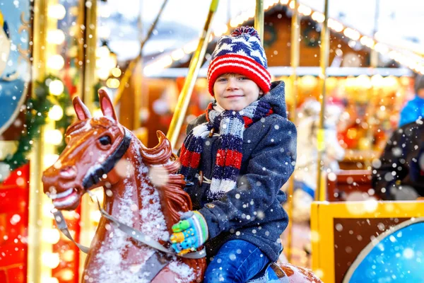 Adorable little kid boy riding on a merry go round carousel horse at Christmas funfair or market, outdoors. Happy child having fun on traditional family xmas market in Cologne, Germany — Stock Photo, Image