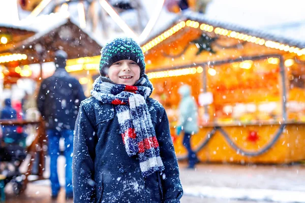 Piccolo ragazzo carino divertirsi sul tradizionale mercato di Natale tedesco durante la forte nevicata.. Bambino felice godendo del tradizionale mercato familiare in Germania, Dresda. Ragazzo ridente in vestiti colorati — Foto Stock