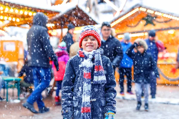 Little cute kid boy having fun on traditional German Christmas market during strong snowfall.. Happy child enjoying traditional family market in Germany, Dresden. Laughing boy in colorful clothes — Stock Photo, Image