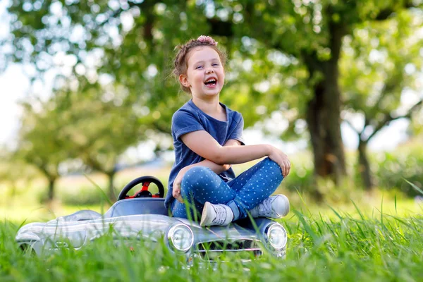 Petite fille d'âge préscolaire conduisant une grosse voiture jouet et s'amusant à conduire dans la nature — Photo