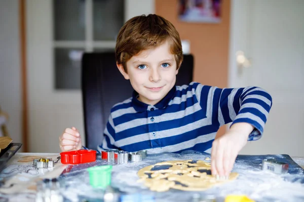 Divertente felice ragazzo della scuola sano cottura biscotti di Natale pan di zenzero a casa. Adorabile bambino biondo che si diverte in cucina domestica. Tempo libero tradizionale con i bambini a Natale. — Foto Stock