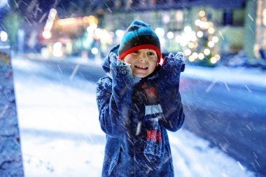 Renkli giysiler içinde kar yağarken dışarıda oynayan komik küçük çocuk. Soğuk karlı günlerde, kışın çocuklarla aktif eğlence. Almanya 'daki Noel pazarında mutlu sağlıklı bir çocuk.