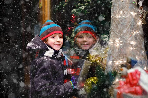 Menino da escola saudável bonito pouco no mercado de Natal. Criança feliz engraçada na moda roupas de inverno fazendo compras de janela decoradas com presentes, árvore de xmas. Neve a cair, neve a cair — Fotografia de Stock