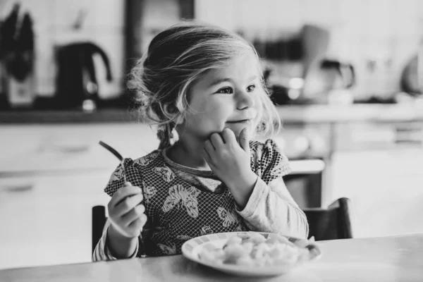 Lief peutermeisje dat gezonde gebakken aardappelen eet als lunch. Schattig vrolijk baby kind in kleurrijke kleding zittend in de keuken van huis, kinderopvang of kinderkamer. Kind eet groenten. — Stockfoto