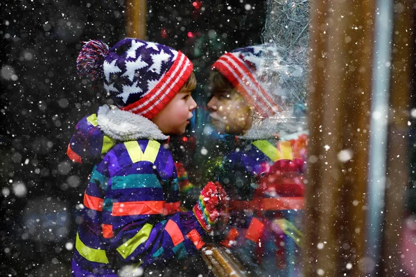 Menino da escola saudável bonito pouco no mercado de Natal. Criança feliz engraçada na moda roupas de inverno fazendo compras de janela decoradas com presentes, árvore de xmas. Neve a cair, neve a cair — Fotografia de Stock