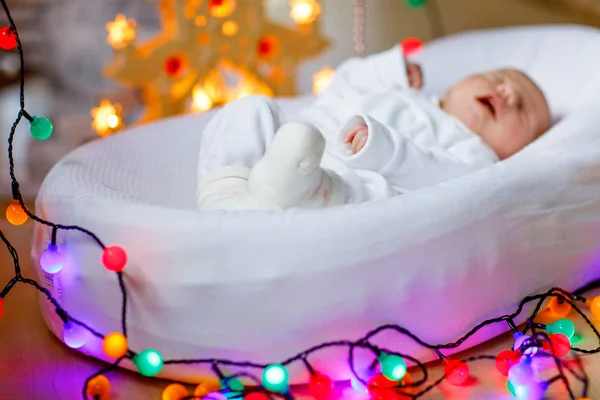 Bebé recién nacido de una semana durmiendo cerca del árbol de Navidad con luces de guirnalda de colores en el fondo. Primer plano del niño lindo, niña, concéntrate en los pies. Familia, Navidad, nacimiento, nueva vida . — Foto de Stock