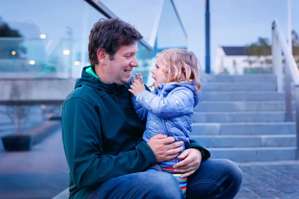 Beautiful portrait of cute little toddler girl with father. Happy baby child hugging with dad. Lovely family of man and daughter. Outdoors at the dusk. — Stock Photo, Image