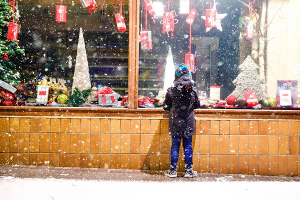 Noel pazarındaki şirin, sağlıklı okul çocuğu. Moda kışı kıyafetleri içinde, hediyelerle süslenmiş vitrin alışverişi yapan neşeli çocuk, xmas ağacı. Kar yağıyor, kar yağıyor. — Stok fotoğraf