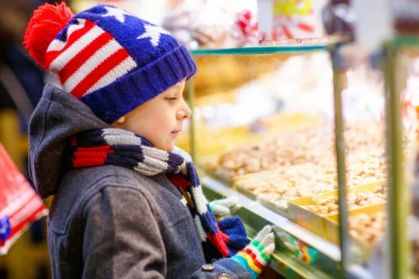 Pequeno menino bonito perto doce stand com pão de gengibre e nozes. Criança feliz no mercado de Natal na Alemanha. Lazer tradicional para famílias em xmas. Férias, celebração, tradição, infância — Fotografia de Stock