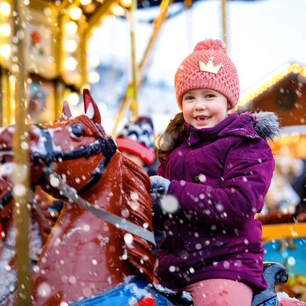 Adorable little kid girl riding on a merry go round carousel horse at Christmas funfair or market, outdoors. Happy child having fun on traditional family xmas market in Nuremberg, Germany.. — Stock Photo, Image