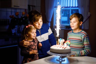 Üçüncü yaş gününü kutlayan sevimli küçük kız. Küçük kız kardeş ve iki erkek kardeş pastaya mum üflüyorlar. Üç çocuklu sağlıklı bir aile portresi.