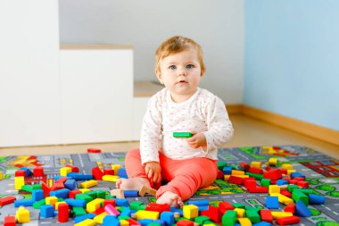 Eğitici oyuncaklarla oynayan sevimli bir kız bebek. Mutlu sağlıklı bir çocuk, evdeki renkli tahta bloklarla eğleniyor. Bebek öğrenme renkleri ve biçimleri