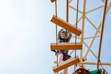 Küçük mutlu çocuk yüksek ip parkuruna tırmanıyor. Aktif çocuk, aile tatillerinde macera ve aksiyon yaşıyor. Cesur çocuklar için meydan okuma.