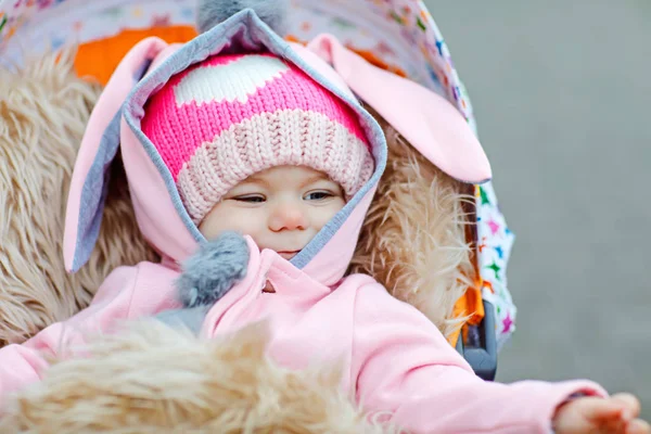 Carino piccola bella bambina seduta nella carrozzina o passeggino il giorno d'autunno. Felice bambino sorridente in abiti caldi, moda elegante cappotto bambino. Bambino sano che va a fare una passeggiata all'aria aperta con i genitori — Foto Stock