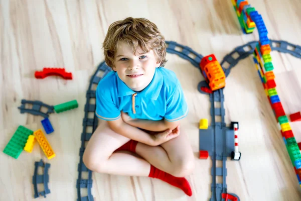 Pequeño niño rubio jugando con bloques de plástico de colores y la creación de la estación de tren — Foto de Stock