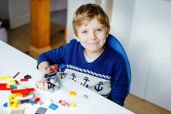 Malé blonďaté dítě, co si hraje se spoustou barevných plastikových bloků. Roztomilá školák se baví s budováním a vytvářením robotů. Tvůrčí volný čas moderní technické a robotické. — Stock fotografie