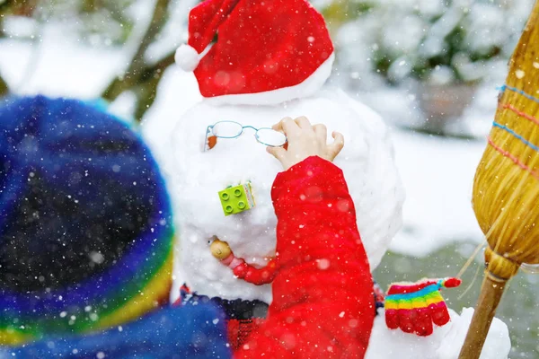 Little kid putting eye glasses on snowman. Close-up. child having fun with first snow in winter — Stock Photo, Image