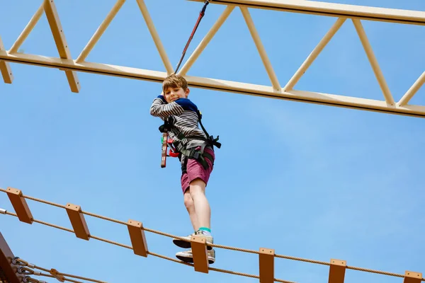 Rapazinho feliz a subir no trilho da corda alta. Criança ativa fazendo aventura e ação em férias em família. Desafio para crianças corajosas . — Fotografia de Stock