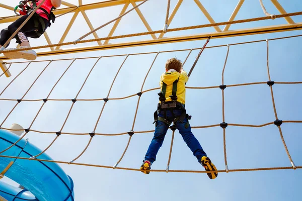 快乐的小男孩爬上了高绳的跑道. 在家庭度假方面,孩子们积极地进行冒险和行动. 勇敢孩子的挑战. — 图库照片