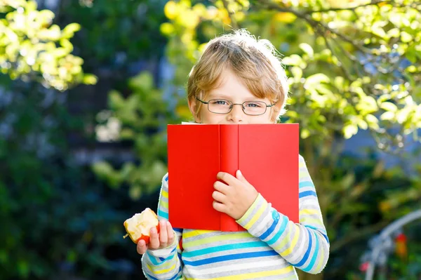 Piccolo bambino felice in età prescolare con occhiali, libri, mela e zaino il suo primo giorno di scuola o asilo nido. Bambino sano divertente all'aperto nella calda giornata di sole, torna al concetto di scuola. Ragazzo ridente. — Foto Stock