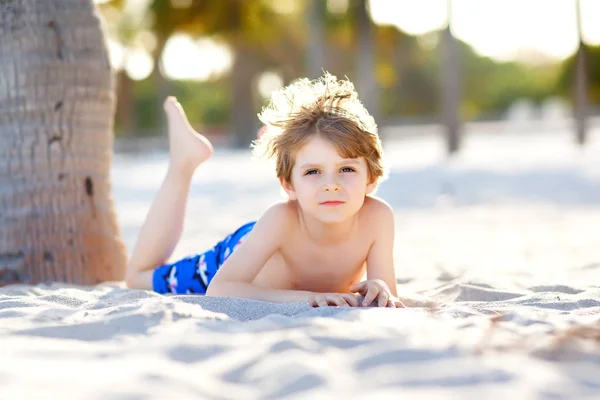 Niño rubio divirtiéndose en la playa de Miami, Key Biscayne. Feliz niño lindo saludable jugando con arena y corriendo cerca del océano. Palmeras, casa de seguridad y arena blanca. Con luz brillante cálida y soleada — Foto de Stock