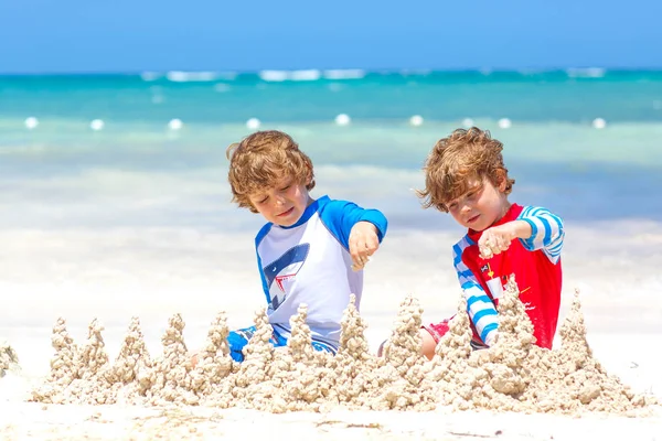 Twee kleine jongens die plezier hebben met het bouwen van een zandkasteel op tropisch strand op het eiland. Gezonde kinderen die samen spelen tijdens hun vakantie. Tweelingen, gelukkige broers lachen en glimlachen — Stockfoto