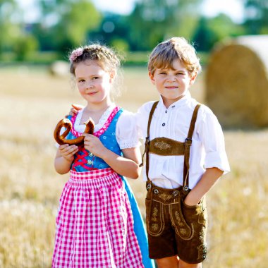Buğday tarlasında geleneksel Bavyera kostümlü iki çocuk. Alman çocukları Ekim Festivali sırasında ekmek ve simit yiyorlar. Almanya 'da yaz aylarında erkek ve kız saman balyalarında oynuyorlar..