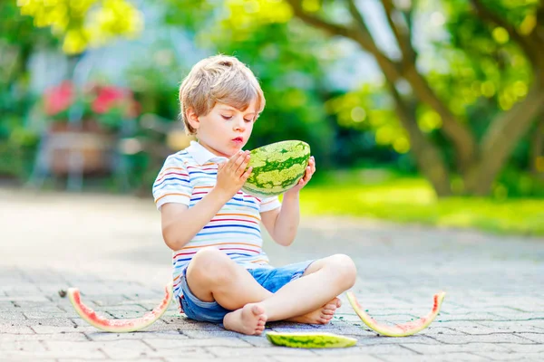 Adorable little preschool kid boy with blond hairs eating watermelon in summer garden. Funny happy child smiling and tasting healthy fruit snack on sunny day — Stock Photo, Image