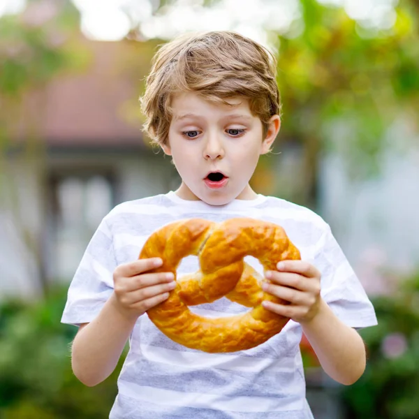 愛らしい子供の男の子は巨大な大規模な野蛮ドイツ語のプレッツェルを食べる。伝統的なパンを楽しむ幸せな金髪の子供。幸せな子供のための健康食品 — ストック写真