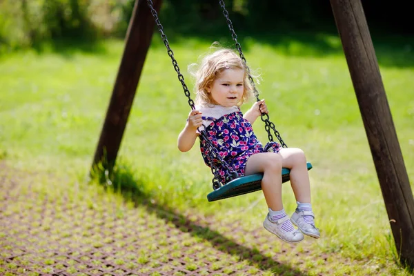 Dziewczyna ładny śliczny maluch kołysanie na plac zabaw. Szczęśliwy uśmiechający się dziecko dziecko siedzi w łańcuchu swing. Aktywne dziecko na słoneczny letni dzień poza — Zdjęcie stockowe