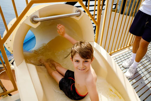 Piccolo ragazzo felice che scivola sul tubo dell'acquascivolo nel parco del resort. Bambino sano divertirsi . — Foto Stock