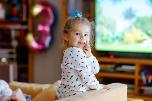 Leuke kleine peuter meisje in nachtkleding pyjama kijken cartoons of film op tv. Gelukkig gezond baby kind thuis. — Stockfoto