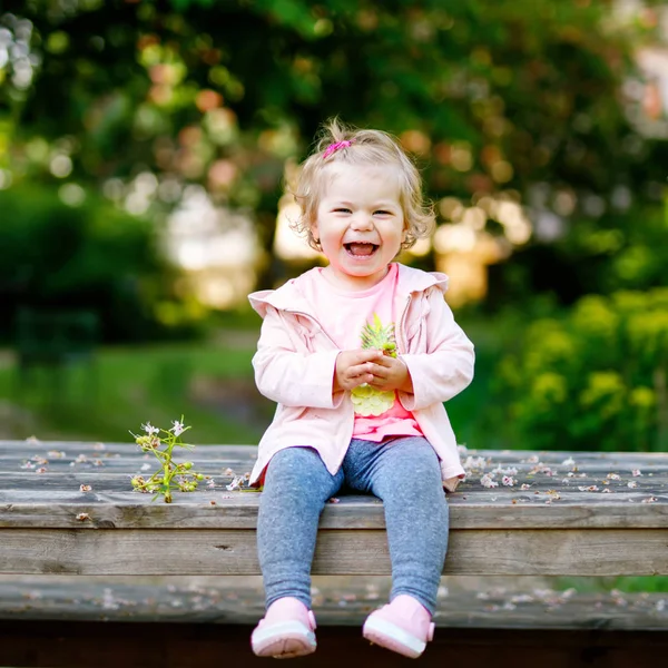 Leuk schattig peuter meisje speelt met bloeiende kastanje bloemen. Baby kindje gaan voor een wandeling op zonnige dag. Gelukkig gezond kind in kleurrijke kleding — Stockfoto