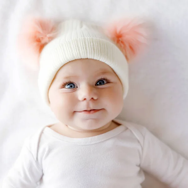 Lindo niño adorable bebé con sombrero blanco cálido y rosa con lindas bobbles. Niña feliz sobre fondo blanco y mirando a la cámara. Primer plano para vacaciones de Navidad y concepto familiar —  Fotos de Stock