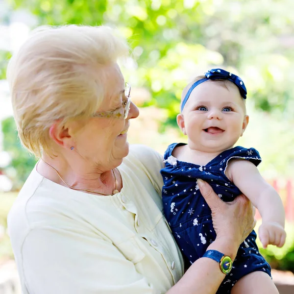 Słodka dziewczynka z babcią w letni dzień w ogrodzie. Szczęśliwa seniorka trzymająca uśmiechnięte dziecko na ramieniu — Zdjęcie stockowe