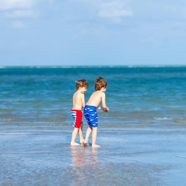 Two little kids boys having fun on tropical beach, happy best friends playing, friendship concept. Siblings brothers, twins in family look with palms on background. Family vacations on ocean. — Stock Photo, Image