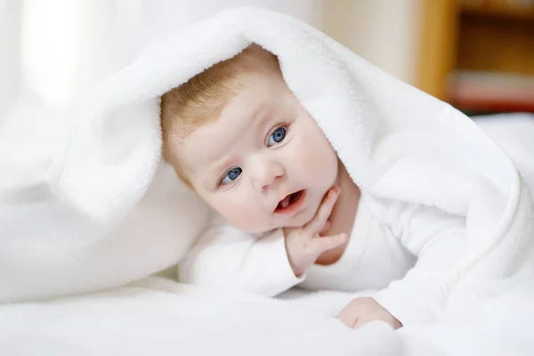 Κοριτσάκι με μπλε μάτια που φοράει λευκή πετσέτα ή κουβέρτα σε λευκό ηλιόλουστο υπνοδωμάτιο. Νεογνό παιδί χαλαρώνει στο κρεβάτι. Βρεφοκομείο για παιδιά. Υφάσματα και κρεβάτια για παιδιά. Ευτυχισμένο χαριτωμένο νεογέννητο κορίτσι ή αγόρι. — Φωτογραφία Αρχείου