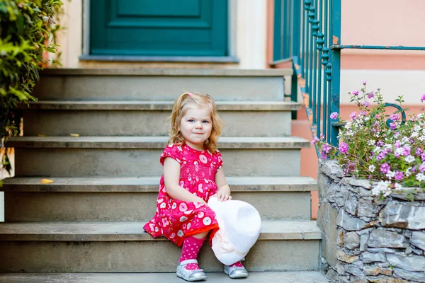 Porträtt av vacker liten gorgeus härlig småbarn flicka i rosa sommar titta kläder, mode klänning, knästrumpor och hatt. Glad frisk baby barn poserar framför färgglada hus. — Stockfoto