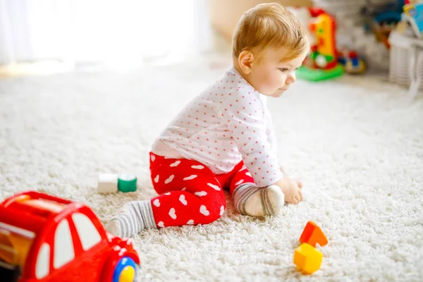Schattig leuk mooie babymeisje spelen met houten onderwijsspeelgoed thuis of kwekerij. Gezonde happy peuter met kleurrijke rode auto binnenshuis. kinderen leren kleuren en vormen — Stockfoto