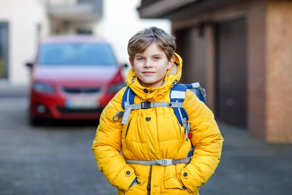 Chłopiec z podstawówki, idący do szkoły. Portret szczęśliwego dziecka na ulicy z korkami. Student w żółtej kurtce i plecaku w kolorowe ubrania zimowe. — Zdjęcie stockowe